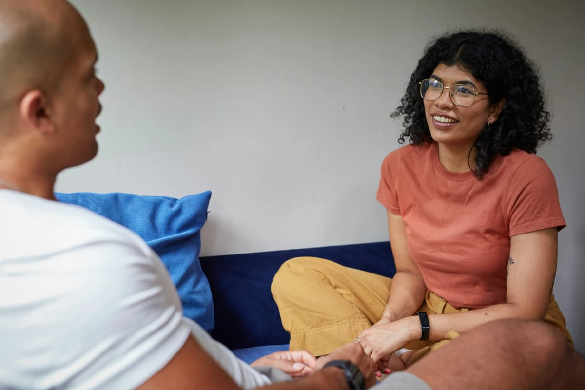 a black woman in a red shirt talking to a bald asian man in a white shirt sitting across from each other