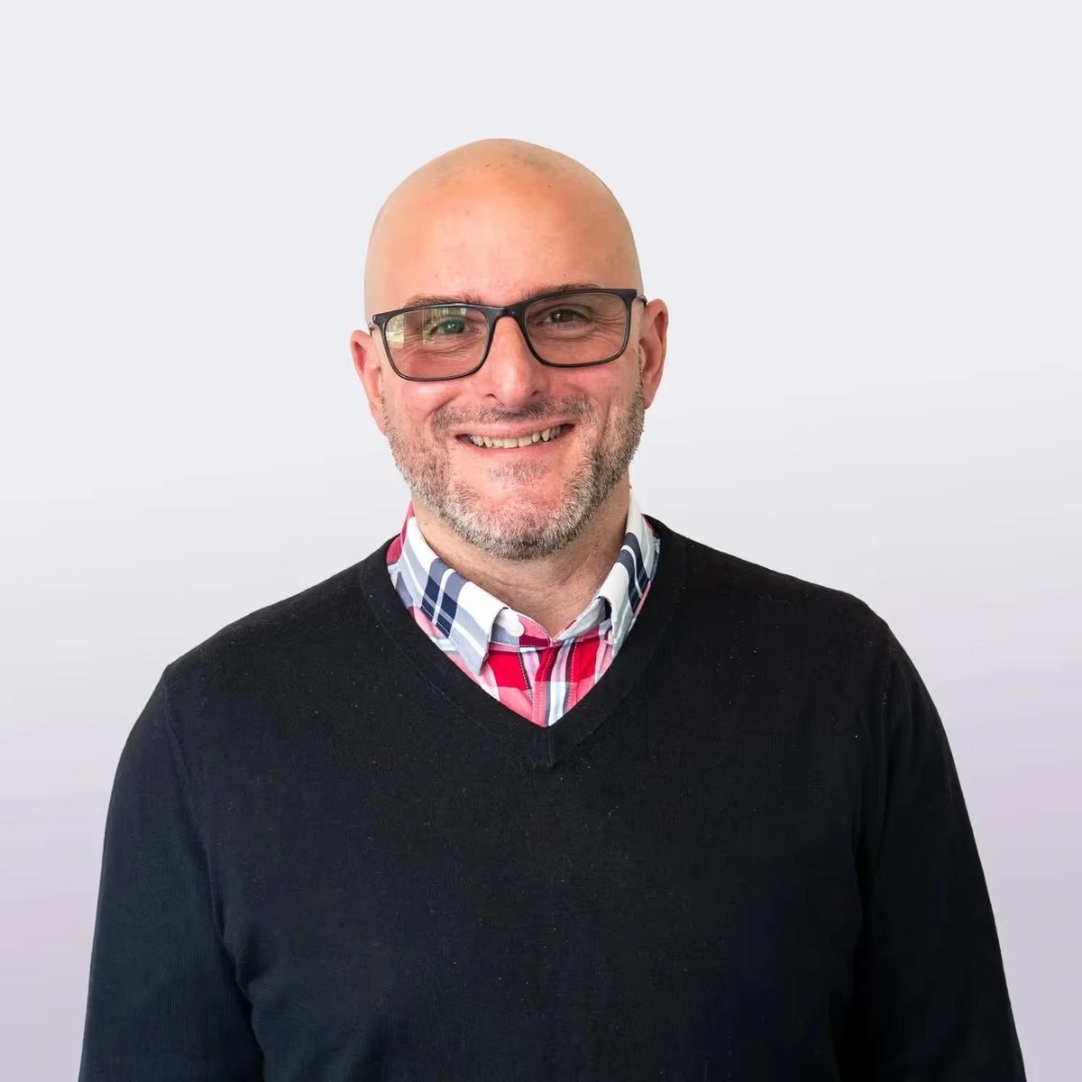 Portrait of Ed Drago, CPS, Advanced-Level WRAP Facilitator at the Institute@MHP, wearing a plaid shirt and smiling against a neutral background, highlighting his dedication to youth peer support and cross-generational mental health advocacy