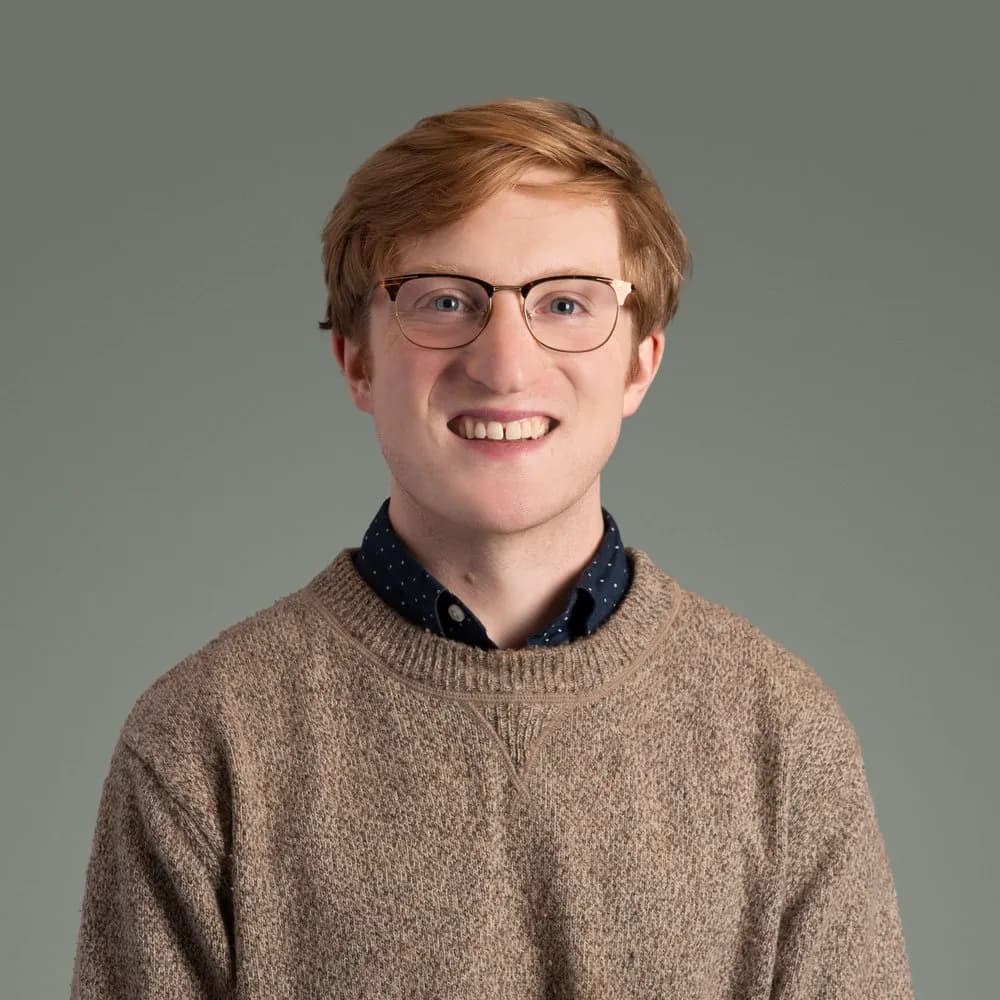 Patrick Montgomery, Program Manager at The Institute, wearing glasses and a tan sweater, smiling against a green background.