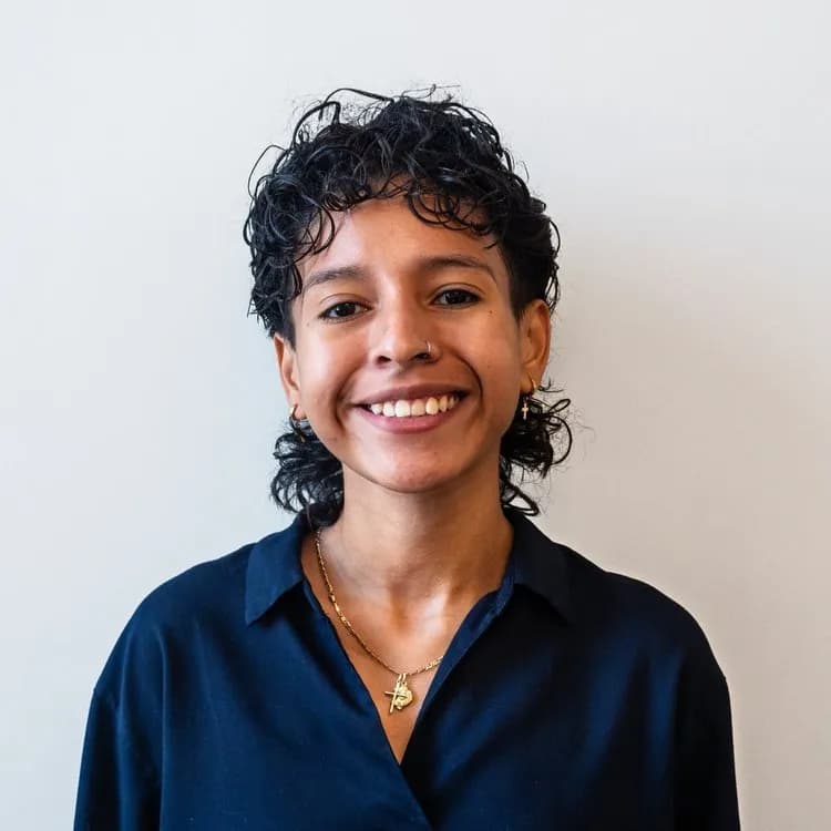 Photo of Mon Ocampo, a Bilingual Learning & Development Specialist at Mental Health Partnerships, smiling in a vibrant top and gray cardigan, reflecting their commitment to Latine mental health advocacy.