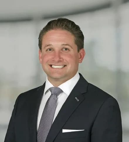 Perry Kaplan, a white man in a dark suit and yellow-striped tie, smiling slightly in a softly lit indoor setting. Board Member at Mental Health Partnerships.