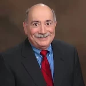 Richard Muhlberg, a white man with short brown hair, smiling in a suit and patterned tie against a neutral brown background. He is the Board Vice-Chair at Mental Health Partnerships.